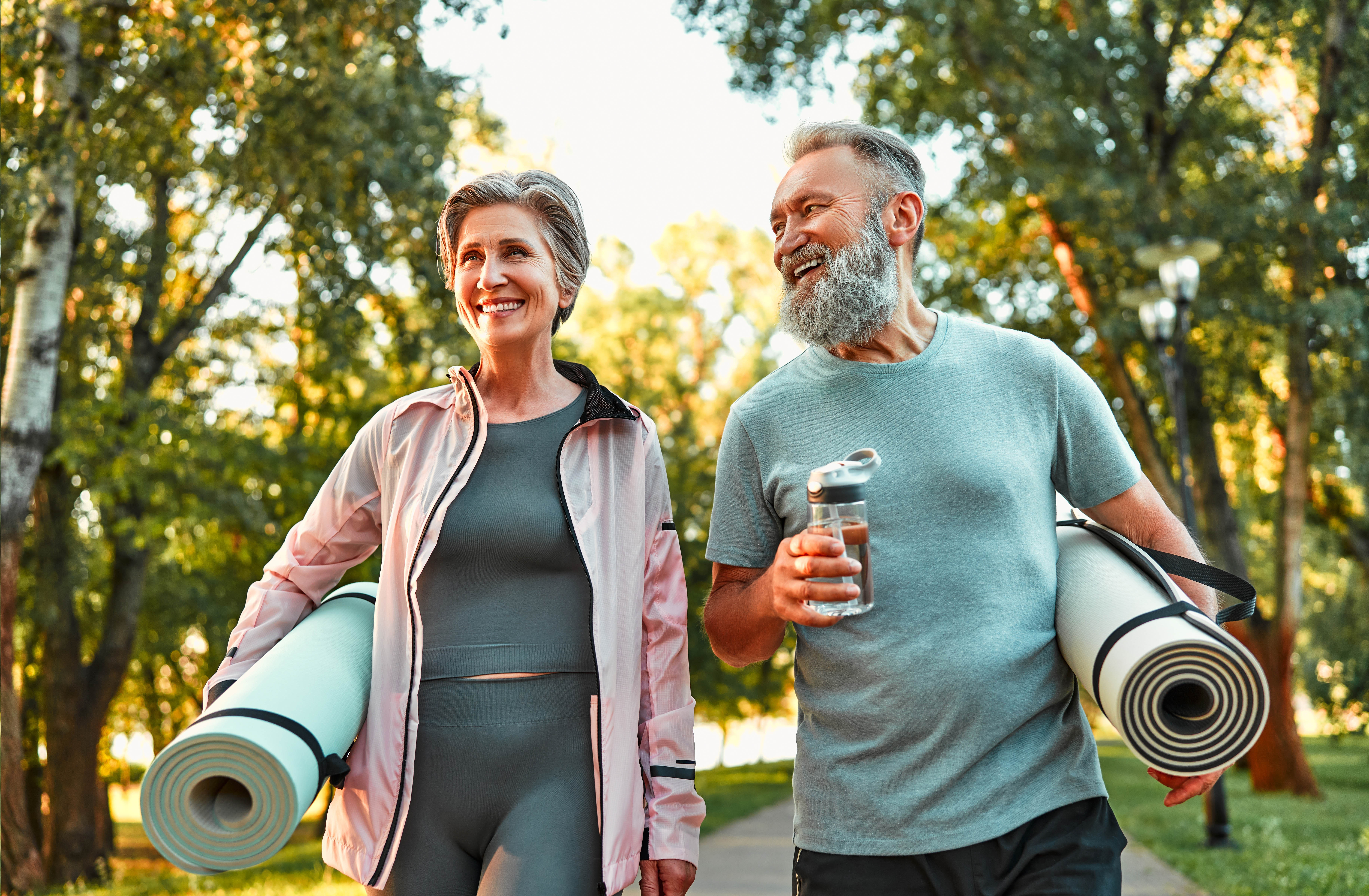 Older couple walking outside with their yoga mats rolled up under their arms